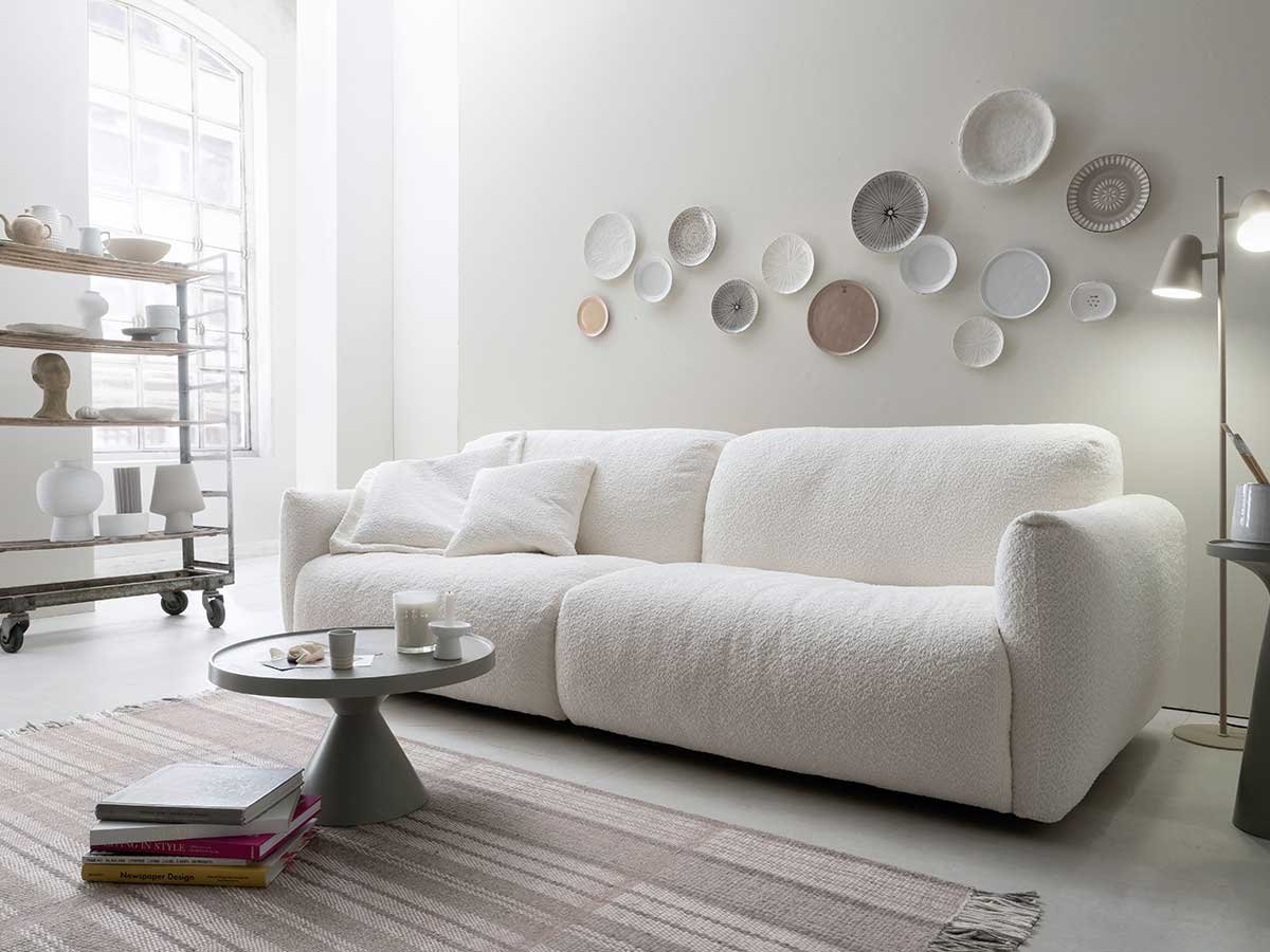 Weißes Sofa mit grauem Couchtisch vor weißer Wand mit Wandtellern