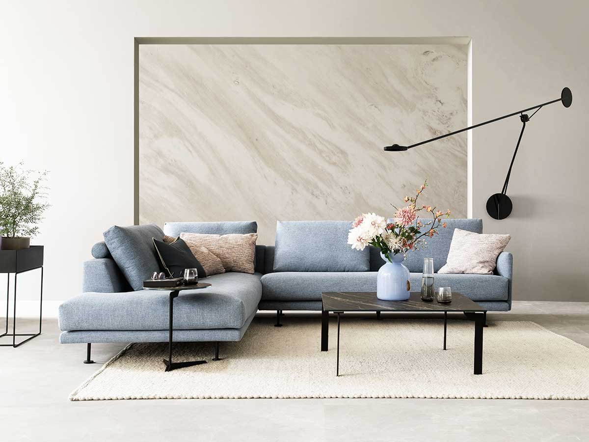 Hellblaue Couch in L-Form vor beiger Marmorwand