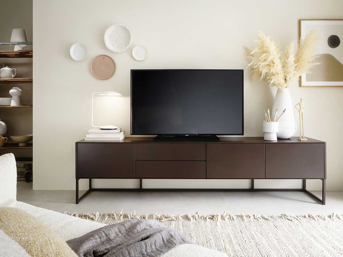 Modernes braunes Lowboard mit TV und weißen Dekoartikeln vor heller Wand mit Wandtellern