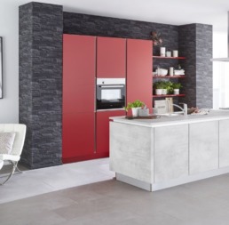 Moderne Inselküche mit roten Elementen an einer grauen Wand. Die Insel ist weiß gehalten.